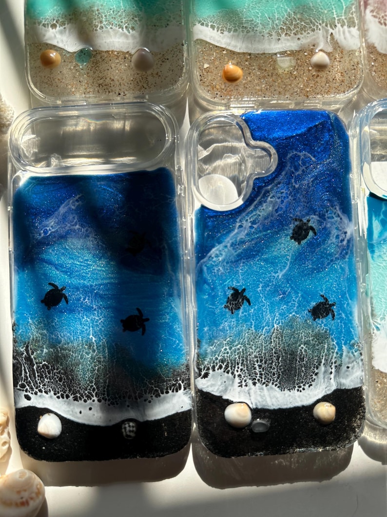 May include: Clear phone cases with ocean-themed resin art. The designs feature dark blue and white waves, black sand, and small sea turtle silhouettes. Some cases include seashells.