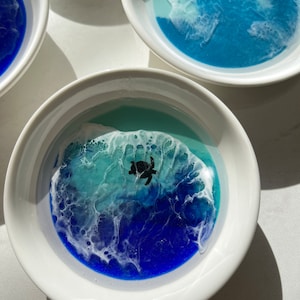 Może przedstawiać: Biała ceramiczna miska z niebiesko-zielonym motywem oceanu w środku. Scena oceaniczna ma białą pianę i czarną sylwetkę żółwia morskiego.