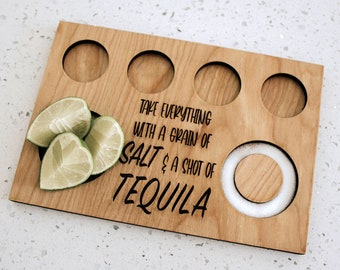 May include: Wooden tequila serving board with four circular cutouts for shot glasses, a central salt holder, and lime wedges. The board is engraved with the phrase "Take everything with a grain of salt & a shot of tequila."