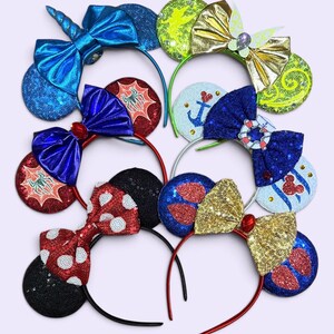 May include: A collection of six decorative headbands featuring various designs including a blue unicorn horn, a gold butterfly, spider webs, a nautical anchor with a life preserver, and red polka dots, all accented with sequins and bows.