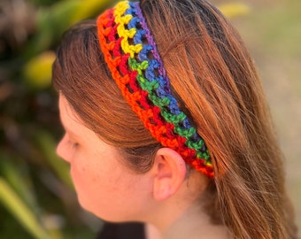 May include: A handmade crochet headband in a vibrant rainbow pattern. The headband features a series of colorful stripes, including red, orange, yellow, green, blue, and purple. The accessory is worn on the head and is made of soft yarn.