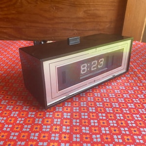 May include: A vintage General Electric digital alarm clock. The clock has a black rectangular body with a silver and white face displaying the time 8:23. The words "LIGHTED DIAL" and "GENERAL ELECTRIC" are printed on the face.