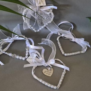 May include: Four heart-shaped ornaments constructed from white ribbon and silver-toned wire, accented with white faux pearls and clear beads. Each heart features a white organza bow and a small tag. One heart displays the text "Anthony & Star 18.04.2025".