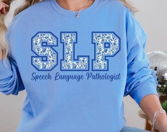 May include: A light blue sweatshirt with the text "SLP" in blue and white floral print. The text "Speech Language Pathologist" is printed below the letters.