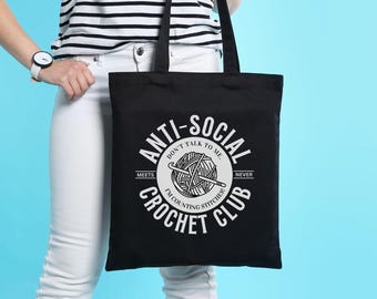 May include: Black tote bag with white text that reads "Anti-Social Crochet Club" with a graphic of a ball of yarn and crochet hook. The text also says "Don't talk to me. Meets I'm counting stitches. Never"