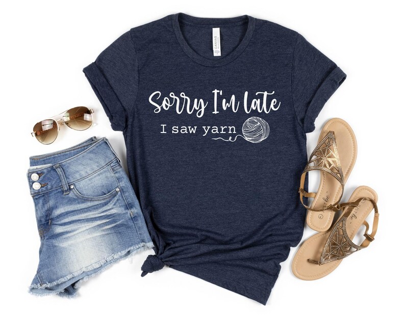 Op de afbeelding: Een marineblauw T-shirt met de tekst "Sorry, ik ben te laat, ik zag garen" en een witte illustratie van een bol garen.