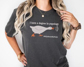 May include: A dark gray t-shirt with a white goose illustration and the text "I have a degree in yapology" and "#SillyGooseSLPClub".