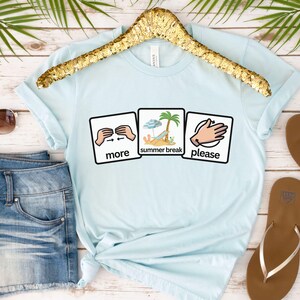 May include: A light blue t-shirt with the words "more summer break please" in a graphic design. The shirt is displayed on a gold hanger, with sunglasses, denim shorts, and sandals in the background.