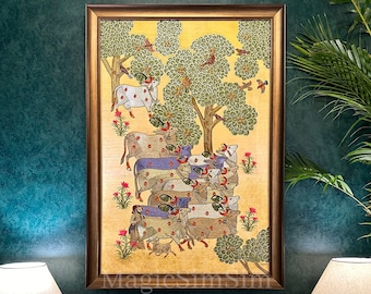 May include: A framed artwork depicting a herd of cows under trees with birds. The cows have patterned coats in shades of brown, white, and purple. The background is a golden yellow, and the frame is a warm brown.
