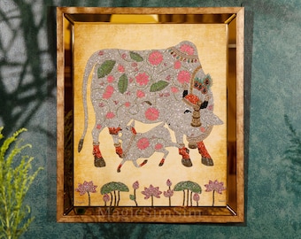May include: A framed artwork depicting a white cow and calf with pink and green floral patterns, surrounded by lotus flowers. The artwork is embellished with sparkling beads and sequins.