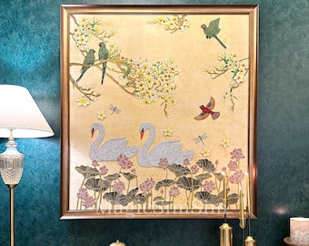 May include: A framed artwork depicting two white swans swimming in a pond with lotus flowers. The background features a golden sky with a blooming cherry blossom tree and several green and red birds.