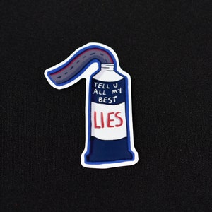 Könnte beinhalten: Ein Aufkleber mit einer blau-weiß-roten Tube mit der Aufschrift "TELL U ALL MY BEST LIES". Ein Straßenmuster erstreckt sich aus der Tube. Der Aufkleber befindet sich auf schwarzem Hintergrund.