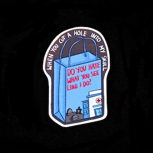 Könnte beinhalten: Ein Aufkleber mit einer blauen Einkaufstaschen-Illustration und dem Text "DO YOU HATE WHAT YOU SEE LIKE I DO?" und "WHEN YOU CUT A HOLE INTO MY SKULL". Der Aufkleber zeigt auch ein Gebäude mit einem roten Kreuz.