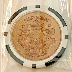 May include: A white and black poker chip with a brown leather insert. The insert features a crest with a crown and the text "Keep Calm and Live On".