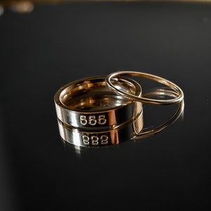 May include: Two gold rings stacked on top of each other. The top ring is thinner and the bottom ring is thicker. The bottom ring has the number "555" engraved on it.