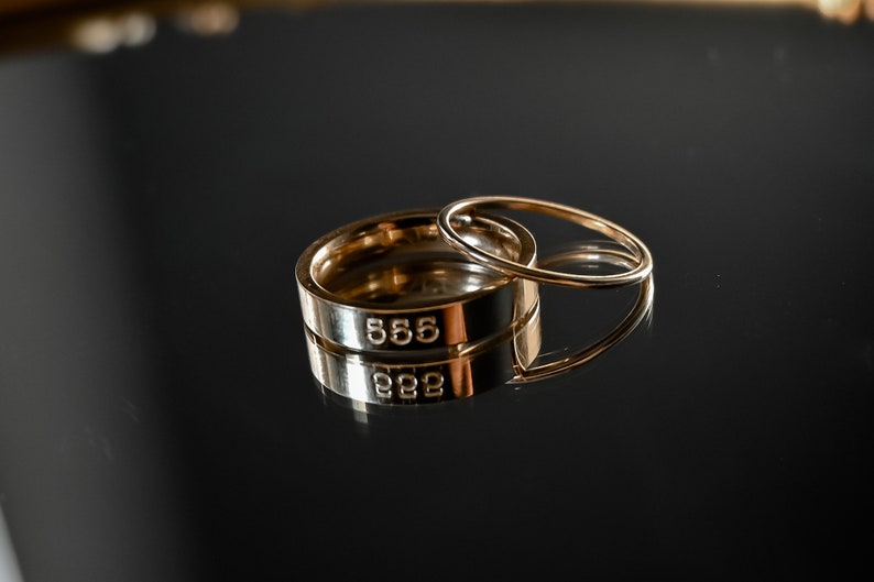 May include: Two gold rings stacked on top of each other. The top ring is thinner and the bottom ring is thicker. The bottom ring has the number "555" engraved on it.