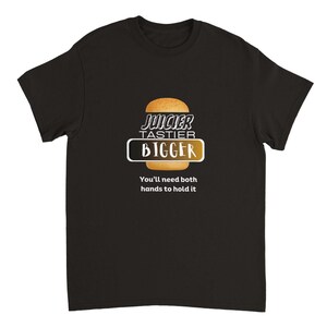 Peut inclure: T-shirt noir avec un graphique d'un gros hamburger et le texte "Juicier Tastier Bigger. You'll need both hands to hold it."