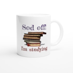 Puede incluir: Taza de cerámica blanca con texto negro y morado que dice "Sod off! I'm studying" y una pila de libros en el fondo.