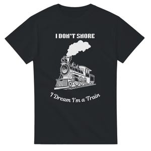 Pode incluir: Camiseta preta com um desenho branco de uma locomotiva a vapor e o texto "I DON'T SNORE" acima. Abaixo, o texto diz "I Dream I'm a Train". O trem está sobre trilhos, com fumaça saindo da chaminé.