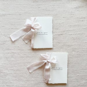 May include: Two small white booklets tied with pink ribbon. The text on the front of the booklets reads "para mi esposo el dia de nuestra boda".
