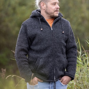 Könnte beinhalten: Ein Mann trägt einen grauen Kapuzenpullover mit Reißverschluss. Er steht in einem Feld mit hohem Gras.