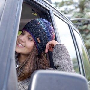 May include: A woman wearing a colorful knitted beanie with a black and gray pattern. She is sitting in a car and looking out the window.