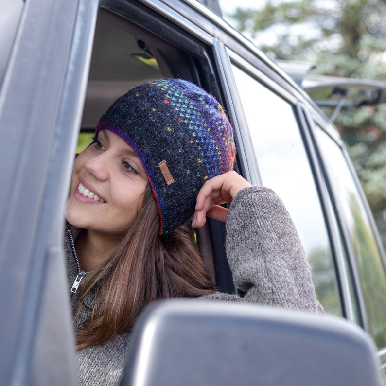May include: A woman wearing a colorful knitted beanie with a black and gray pattern. She is sitting in a car and looking out the window.