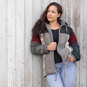Könnte beinhalten: Eine Kapuzenjacke im Patchwork-Design in Grau-, Rot- und Schwarztönen. Die Jacke hat einen Reißverschluss und Holzknebel. Die Ärmel haben gestreifte und einfarbige Farbblöcke. Die Jacke ist aus einem dicken, strukturierten Material gefertigt.