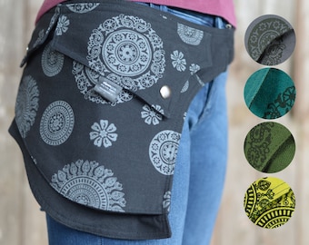 May include: A black fabric hip belt with a large pocket and a silver buckle. The belt is decorated with a silver mandala pattern. The belt is shown being worn over a pair of blue jeans.