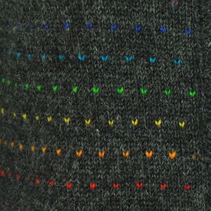 May include: A dark gray knitted fabric with a rainbow pattern of small embroidered hearts. The hearts are arranged in rows, with the colors of the rainbow fading from blue to red.