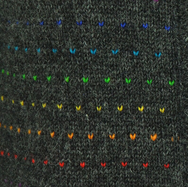 May include: A dark gray knitted fabric with a rainbow pattern of small embroidered hearts. The hearts are arranged in rows, with the colors of the rainbow fading from blue to red.