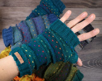 May include: Hand-knitted fingerless gloves in various shades of blue, green, and yellow, with colorful speckles. The gloves have a ribbed cuff and a small leather tag. The background is a wooden surface.