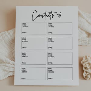 Puede incluir: Un bloc de notas blanco para la lista de contactos con la palabra "Contacts" en escritura cursiva. El bloc de notas tiene espacios para el nombre, el teléfono, la dirección y el correo electrónico. Un coral decorativo y un paño blanco están en el fondo.