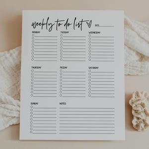 May include: A white weekly to-do list with black text, featuring the days of the week and space for notes. The title "weekly to do list" is in a cursive font. The list is set against a neutral background.