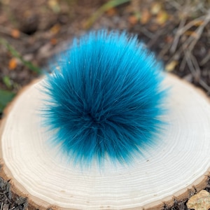 May include: A teal blue faux fur pom pom. The pom pom is fluffy and soft, and it is perfect for adding a touch of colour and texture to any project.