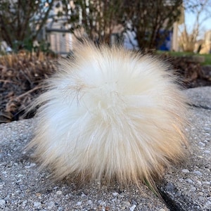 May include: A fluffy white and brown faux fur pom pom. The pom pom is soft and fluffy, and would be perfect for adding a touch of whimsy to a hat or scarf.