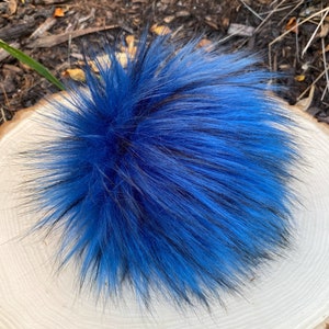 May include: A fluffy blue and black faux fur pom pom. The pom pom is made of soft, synthetic fur and is perfect for adding a touch of whimsy to any project.