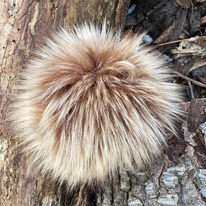 May include: A fluffy brown and white faux fur pom pom. The pom pom is made of soft, plush fur and is perfect for adding a touch of whimsy to any project.