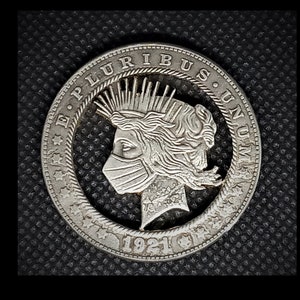 May include: A silver coin with a modified design. The coin features a profile of a person wearing a face mask. The text "E PLURIBUS UNUM" is visible around the edge, along with the year "1921".