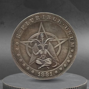 May include: A silver coin featuring a detailed depiction of a goat-like figure within a pentagram, surrounded by the inscription "E PLURIBUS UNUM" and the year "1881". The coin is displayed on a dark, tiered platform.