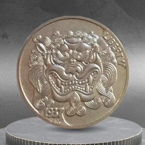 May include: A gold-colored coin featuring a detailed relief of a mythical creature's face, with the word "LIBERTY" visible. The coin is dated 1937 and is displayed on a dark, tiered platform.