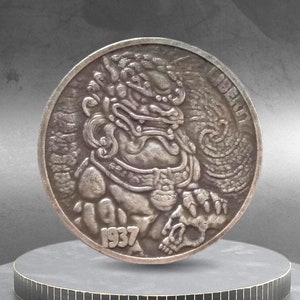 May include: A silver coin featuring a detailed relief of a mythical creature, possibly a guardian lion, with intricate designs. The coin has the year 1937 inscribed and the word "LIBERTY". The coin is displayed on a black and gold tiered stand.