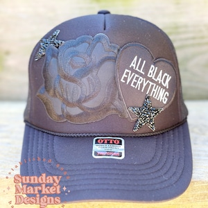 May include: Black trucker hat with a black rose, a black heart with the text "ALL BLACK EVERYTHING" and a black star with rhinestones.