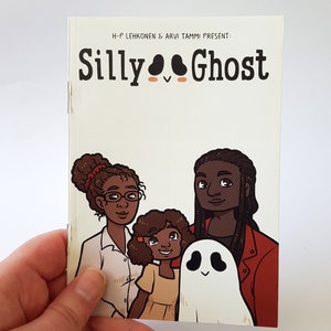 Może przedstawiać: Okładka komiksu z tytułem "Silly Ghost" w pomarańczowym i czarnym kolorze. Na okładce przedstawiona jest rodzina składająca się z trzech osób: kobiety w okularach, mężczyzny z dredami i dziewczynki, wszyscy uśmiechają się. Przed nimi znajduje się biały duch z czarnymi oczami.