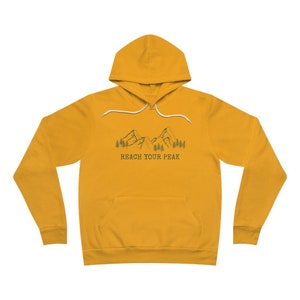 May include: A mustard yellow hoodie with a white drawstring and a graphic of mountains and trees. The text "REACH YOUR PEAK" is printed below the graphic.