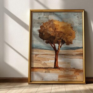 May include: A framed abstract landscape painting featuring a tree with a brown trunk and a full, golden-brown crown. The background has a textured, muted color palette of beige, gray, and blue, with a gold frame. The artwork is leaning against a white wall.