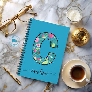 May include: A blue spiral notebook with a floral design letter "C" and the name "caroline" written in cursive.