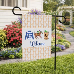 Puede incluir: Una bandera de jard&iacute;n decorativa con un patr&oacute;n de herraduras y gr&aacute;ficos tem&aacute;ticos de carreras. La bandera incluye los colores de un jockey, un caballo y un jinete, y un c&oacute;ctel. La palabra "Welcome" est&aacute; escrita en una fuente cursiva.