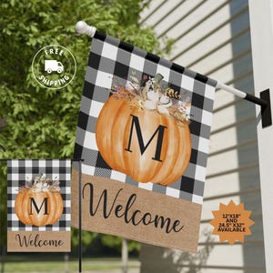 May include: A black and white checkered welcome flag with a pumpkin and the letter "M" in the center. The pumpkin is decorated with fall flowers and leaves. The bottom of the flag has a burlap texture with the word "Welcome" written in black.