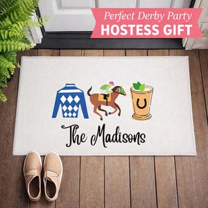 May include: White doormat with a blue and white diamond pattern jockey uniform, a horse and jockey, and a mint julep illustration. The text "The Madisons" is below the illustrations. The text "Perfect Derby Party HOSTESS GIFT" is at the top.